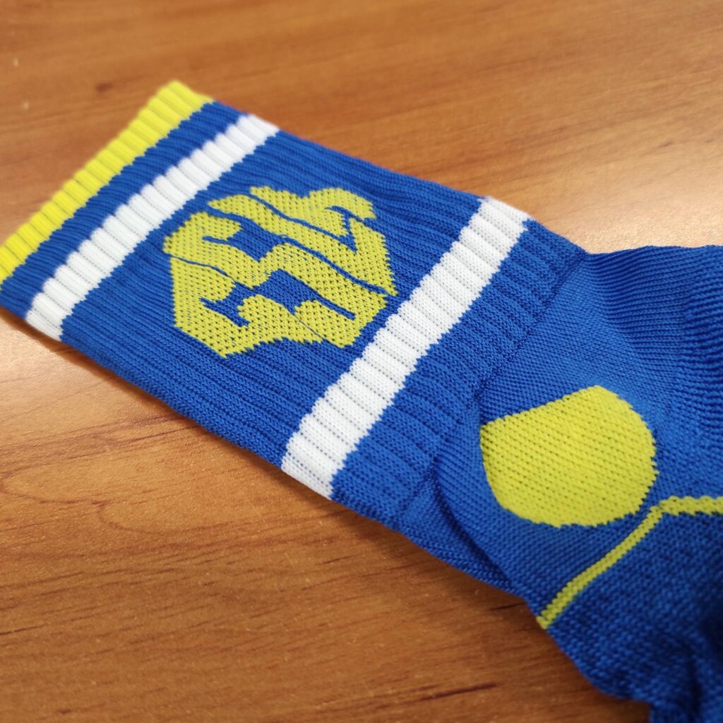 Chaussette de sport bleue et jaune fluo à rayures blanches. Un logo hexagonal stylisé est tricoté sur la tige de la chaussette.