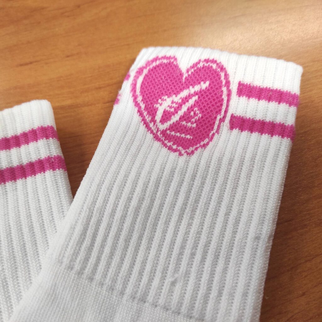 Chaussettes blanches côtelées. Manchette avec un cœur rose vif contenant un symbole blanc stylisé et deux rayures fuchsia.
