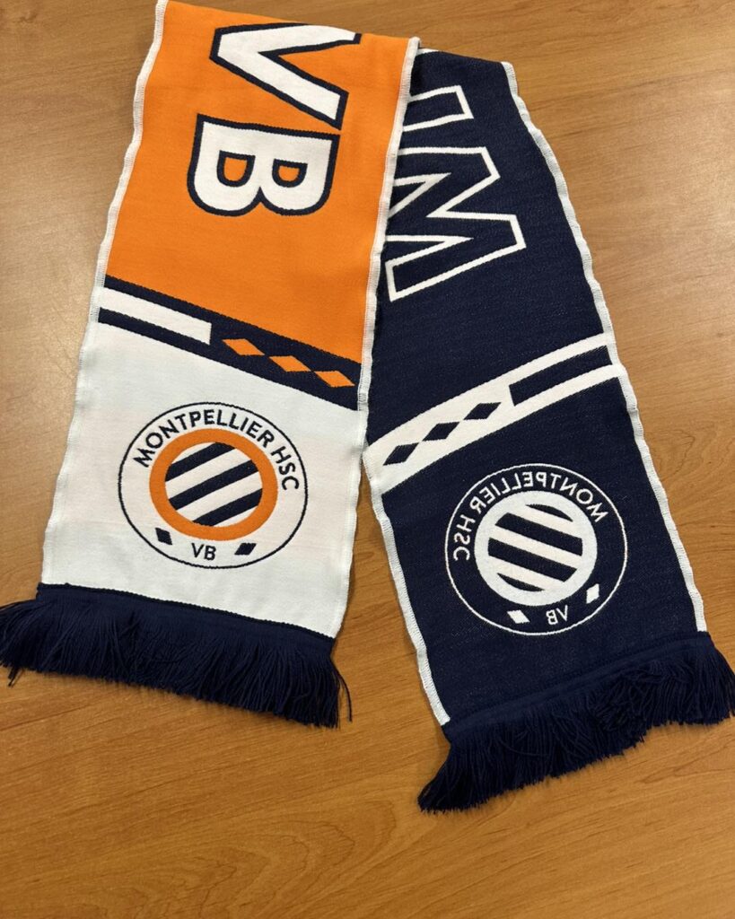 Écharpe supporter Montpellier HSC VB. Bleu marine et orange. Écharpe Montpellier HSC bi-face orange/bleu marine. Grand texte "VB". Logo du club avec franges. Articles de supporter de foot.