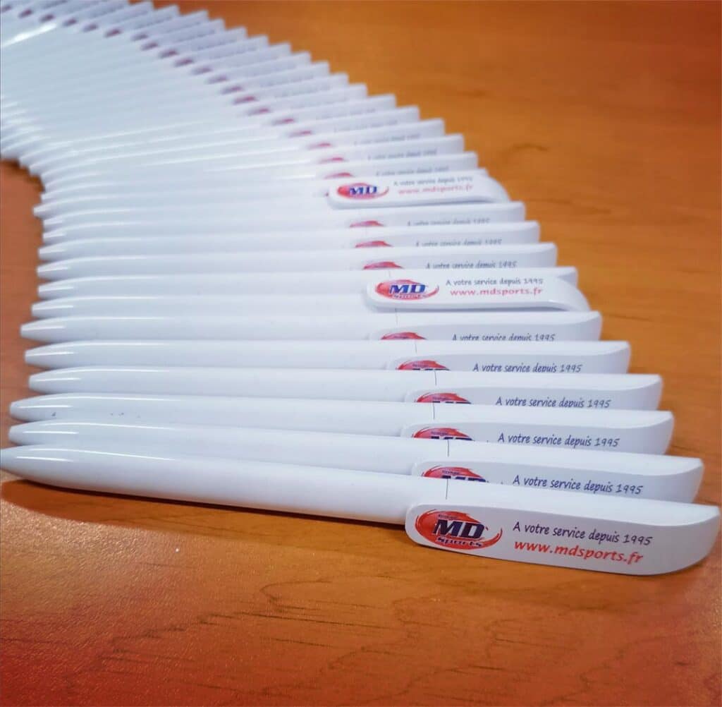 Stylos promotionnels MD Sports – Votre branding efficace. Stylos promotionnels blancs MD Sports alignés en éventail. Texte visible : "À votre service depuis 1995" et "www.mdsports.fr".