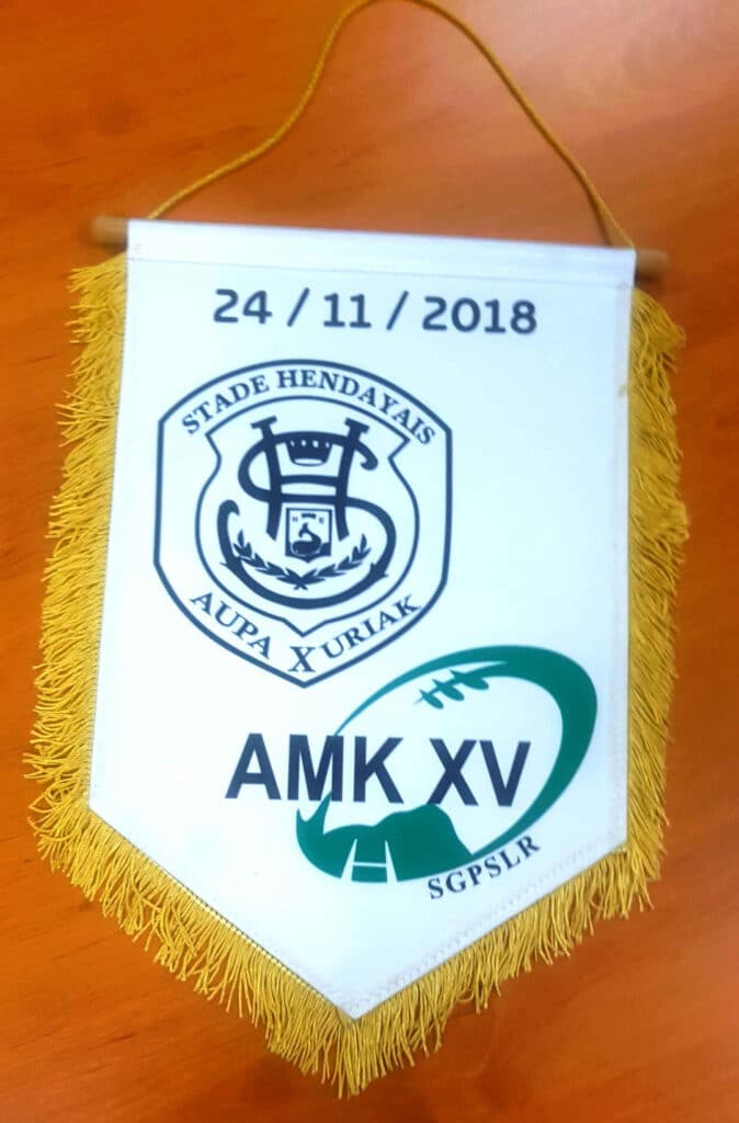 Fanion blanc Stade Hendayais et AMK XV, date 24/11/2018, avec logos et franges jaunes sur bois.