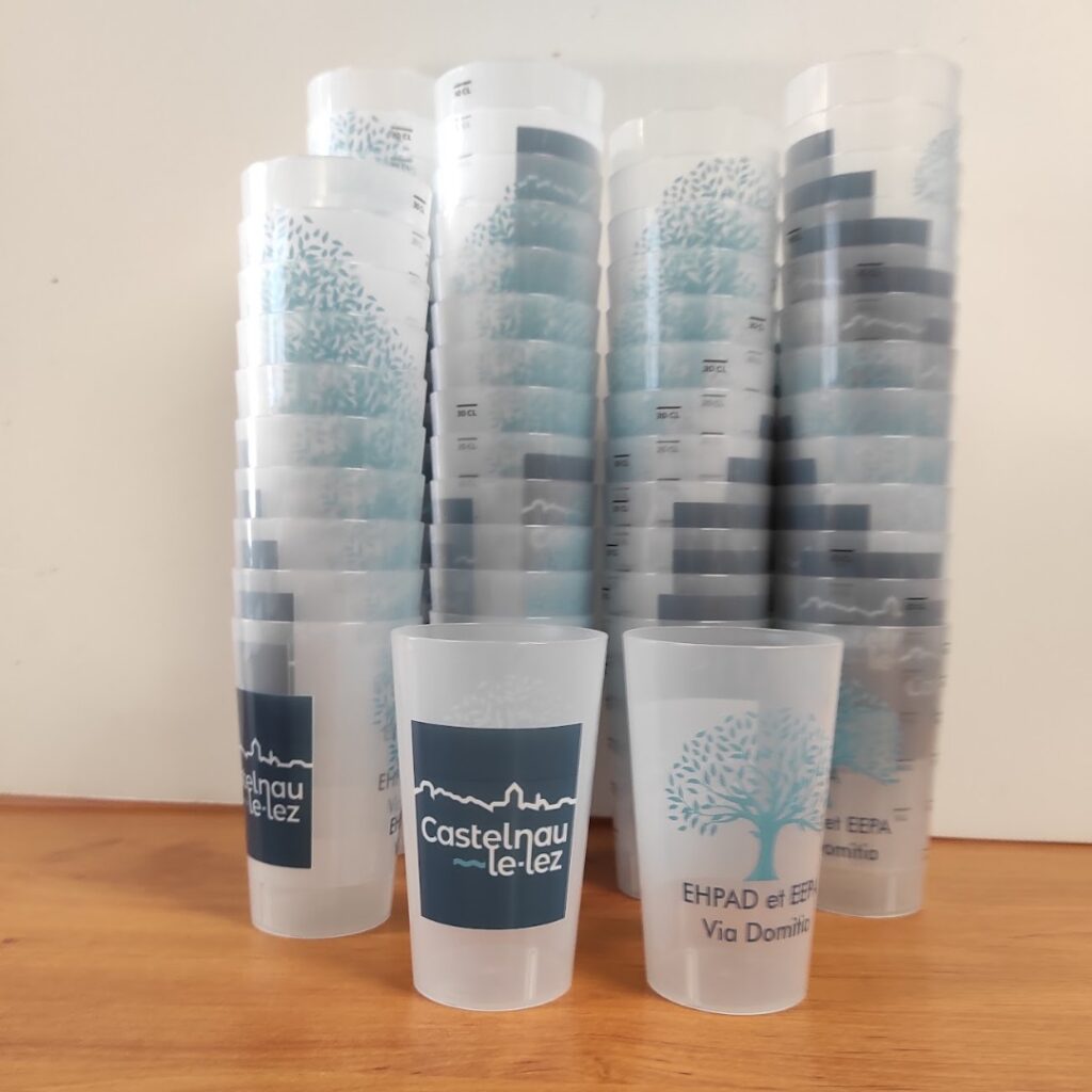 Gobelets réutilisables Castelnau-le-Lez et EHPAD Via Domitia personnalisés, verres plastiques empilés sur bois.